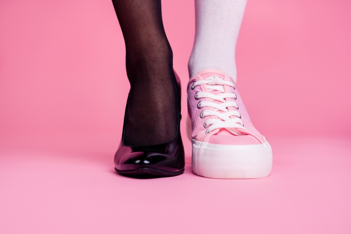 O calçado inadequado é uma das principais causas de calosidades: Getty Images Pernas e sapatos, duas pernas, uma com meias de seda pretas e sapatos de salto pretos e a outra com meias cor-de-rosa e ténis.