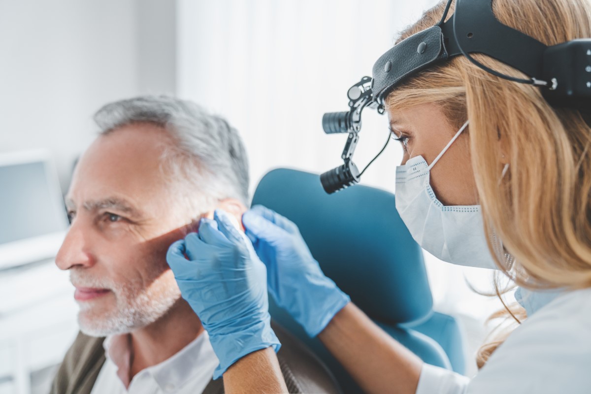 O exame é efectuado por um especialista em otorrinolaringologia. Fonte: Getty Images Exame otorrinolaringológico do ouvido, homem idoso sentado na cadeira de exame e a ser examinado por um médico