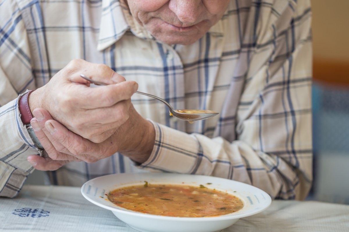O tremor causa problemas nas actividades diárias normais: Getty Images Homem come sopa e segura a mão contra tremores na doença de Parkinson
