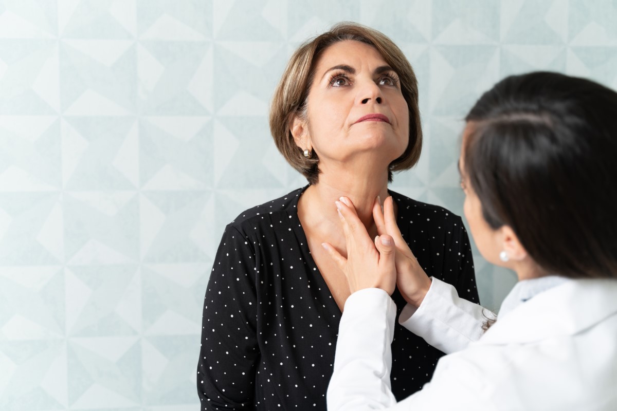 É importante examinar por palpação: Getty Images Médico a palpar a glândula tiroide, mulher idosa sentada em frente