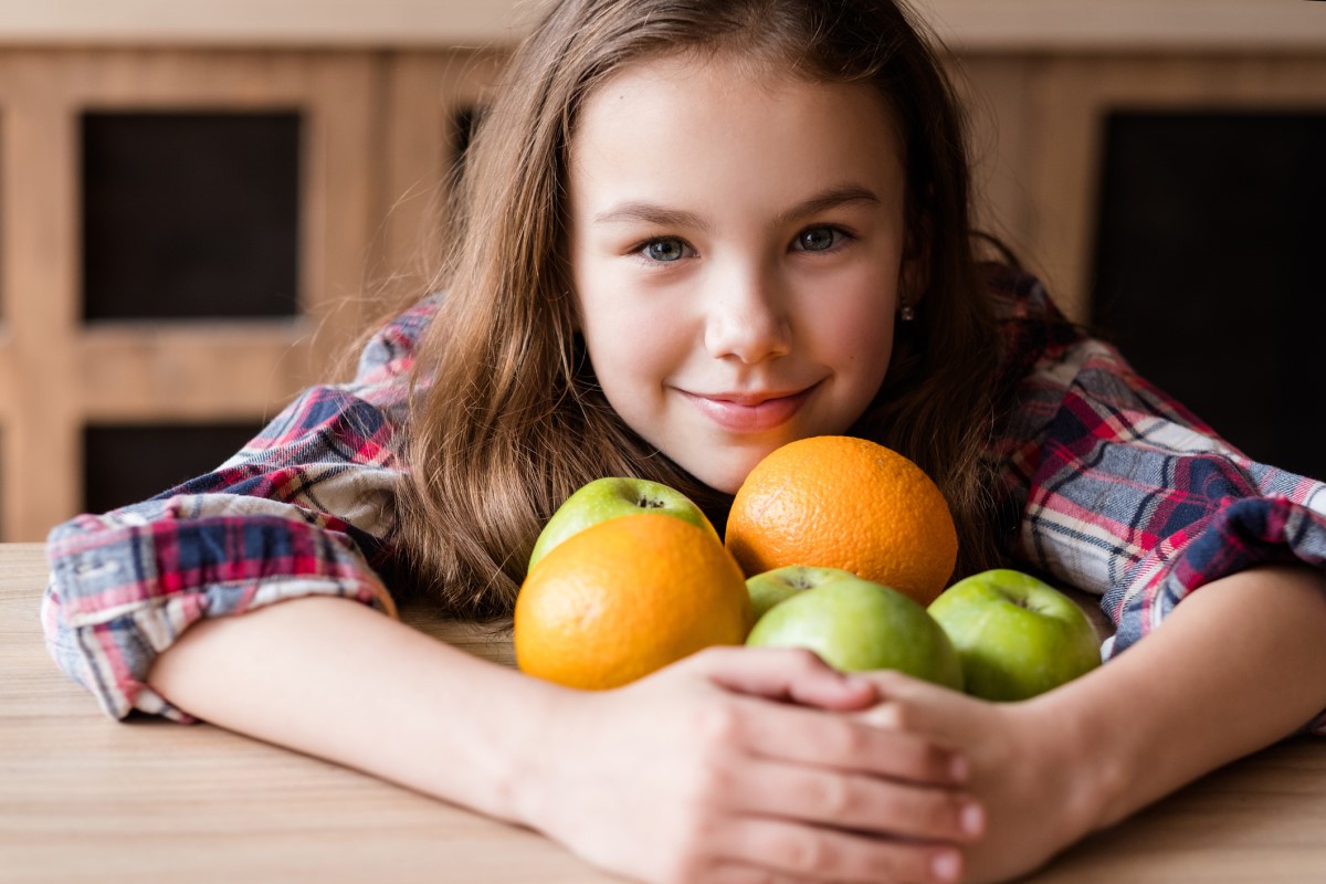 Em cada idade é necessária uma dose diária diferente desta vitamina, sendo as melhores fontes as frutas e os legumes: Getty Images Vitamina C, em frutos, uma criança com laranjas e maçãs nos braços