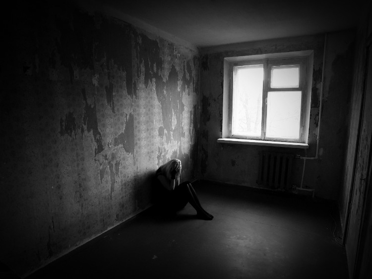 A depressão faz com que as pessoas procurem a solidão: Getty Images uma mulher sentada numa sala escura, encostada à parede, segurando o rosto com as mãos