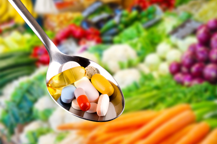 O complexo vitamínico é a base da saúde. Fonte: Getty Images vitaminas em comprimidos numa colher, muitos legumes frescos ao fundo