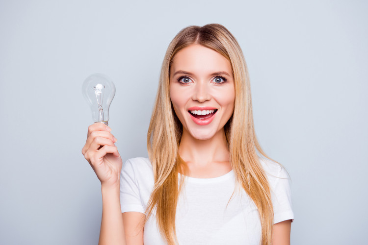 Terapia com luz - fototerapia Fonte: Getty Images mulher risonha de cabelo louro com uma T-shirt branca a segurar uma lâmpada