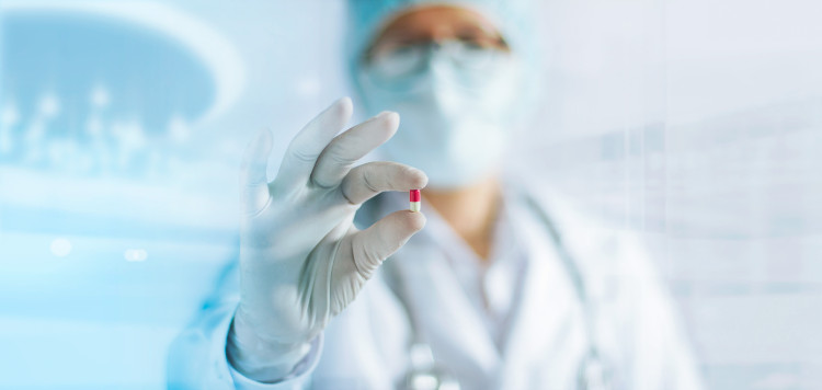 Tratamento conservador das hemorróidas Fonte: Getty Images uma médica de uniforme branco, com um véu no rosto, segurando um comprimido na mão