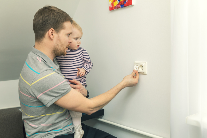 A utilização de tampões de segurança reduz o risco de lesões. Foto: Thinkstock O pai segura uma criança pequena nos braços e fecha a ficha com uma ficha eléctrica