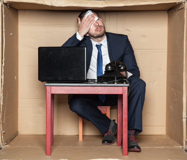 Aumento da carga de trabalho e do stress como causa: Getty Images Homem de negócios sentado a uma secretária numa caixa, espaço apertado, stress no trabalho e aumento da carga de trabalho, computador e telefone, homem a limpar a testa