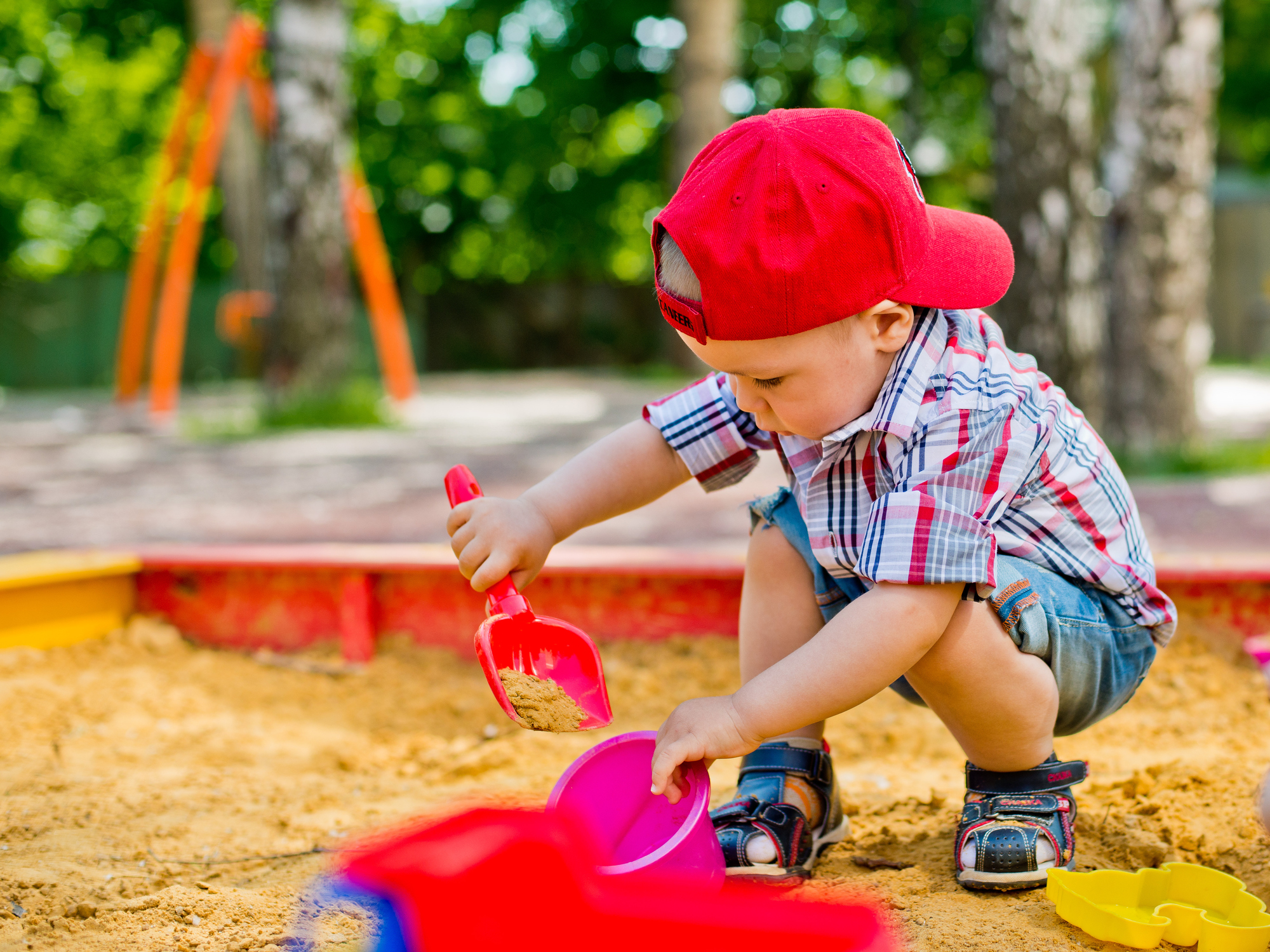 Brincar na areia não desenvolve apenas as capacidades das crianças. Foto: Thinkstock Um rapaz a apanhar areia com uma pá para um balde numa caixa de areia.