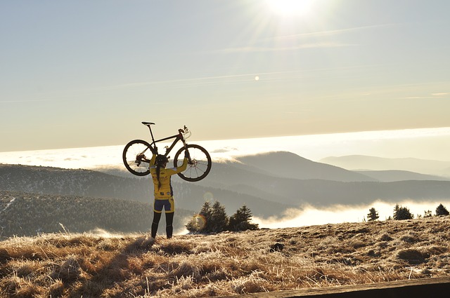 O desporto fortalece o corpo e o espírito. Fonte: Thinkstock Uma ciclista levanta a sua bicicleta acima da cabeça. Ao fundo, há montanhas no nevoeiro.