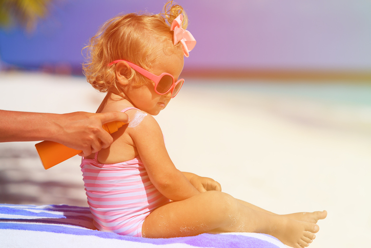 Pense na proteção UV para os seus filhos. Fonte: Thinkstock Uma criança a apanhar banhos de sol, a mãe põe-lhe protetor solar