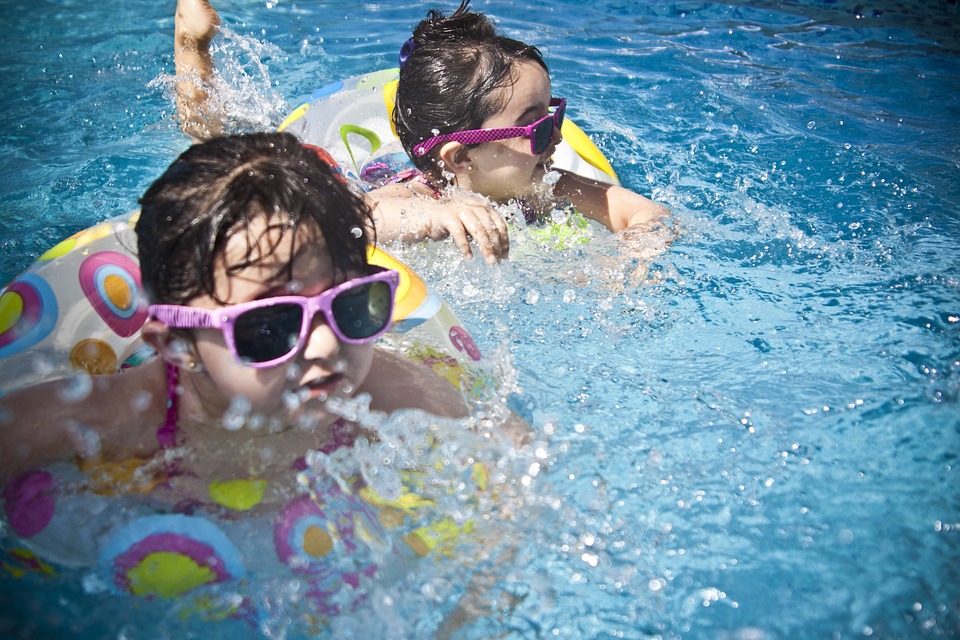 As infecções dos ouvidos afectam especialmente as crianças. Foto: Thinkstock Duas crianças estão a nadar na água, usam óculos de sol com armação cor-de-rosa e estão em bicicletas flutuantes.
