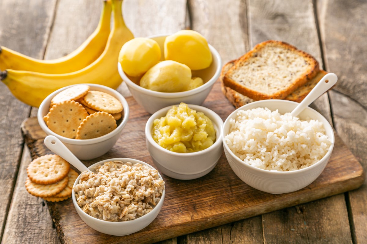 Exemplo de uma dieta adequada para a diarreia aguda Fonte: Getty Images. Exemplo de uma dieta adequada para a diarreia aguda - arroz, batatas, bananas, bolachas, biscoitos, em tigelas e numa tábua de cortar madeira.