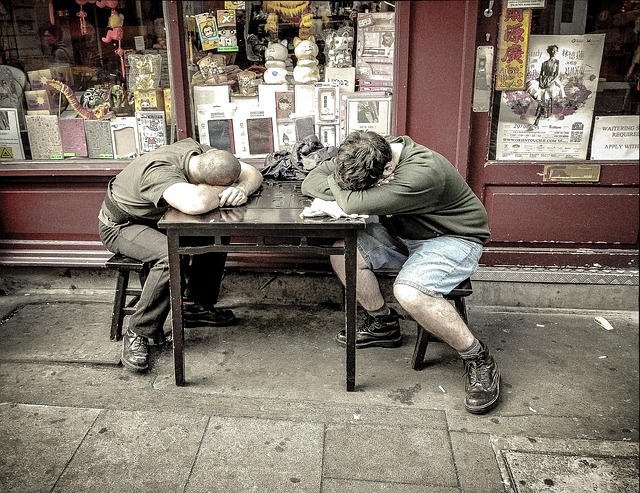 O sono é muito importante para aliviar o stress. Fonte: Thinkstock Dois homens dormem numa mesa à porta da loja. É uma loja antiga.