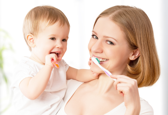 Mesmo com uma limpeza regular, podem formar-se cáries, mas a selagem pode ser uma prevenção eficaz. Fonte: Thinkstock Uma mãe escova os dentes com o seu filho ao colo.