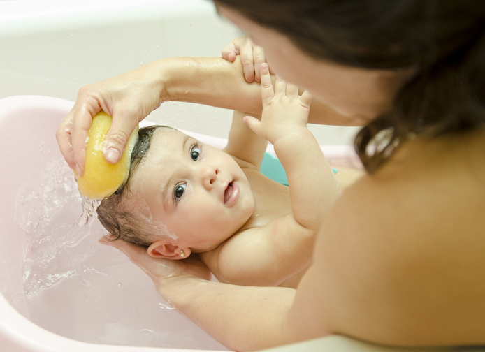Uma alternativa adequada ao arrefecimento físico é um banho morno. Foto: Getty Images Mãe a lavar o seu bebé num banho de esponja