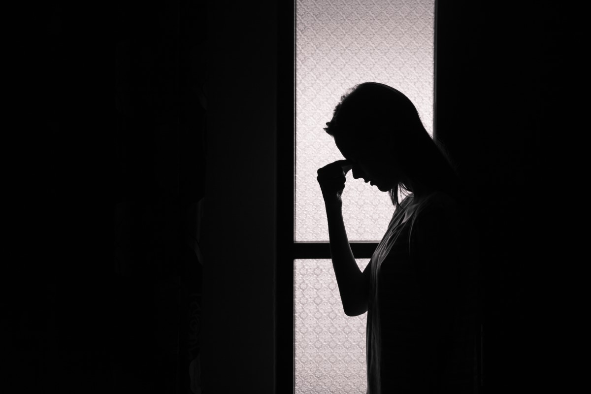Enxaqueca, sensibilidade à luz, mulher de pé num quarto escuro