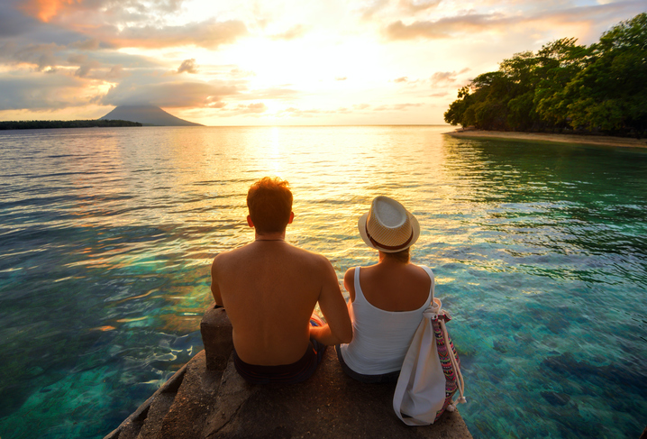 As armadilhas do verão Foto: Thinkstock casal sentado numa rocha junto ao mar ao nascer do sol