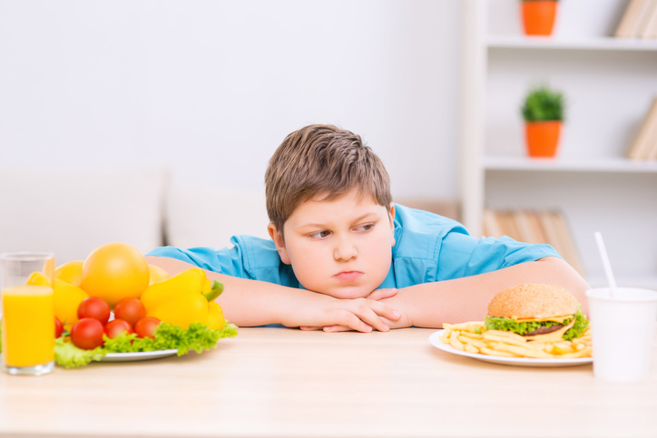 Nenhuma criança come legumes porque são saudáveis, comem-nos porque os pais também gostam de os comer. Foto: Thinkstock Um miúdo gordo entre dois pratos de comida saudável e não saudável.