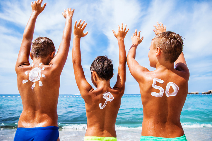 Na infância, escolhemos FPS 50 e 50+. Fonte: Thinkstock Protetor solar para crianças com OF 50, as crianças estão na praia junto ao mar e divertem-se, têm as mãos no ar