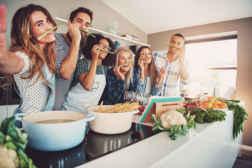 Uma alimentação saudável e de qualidade também contribui para um melhor estado mental. Fonte da foto: Getty Images Pessoas a sorrir enquanto preparam a comida, atrás do fogão.