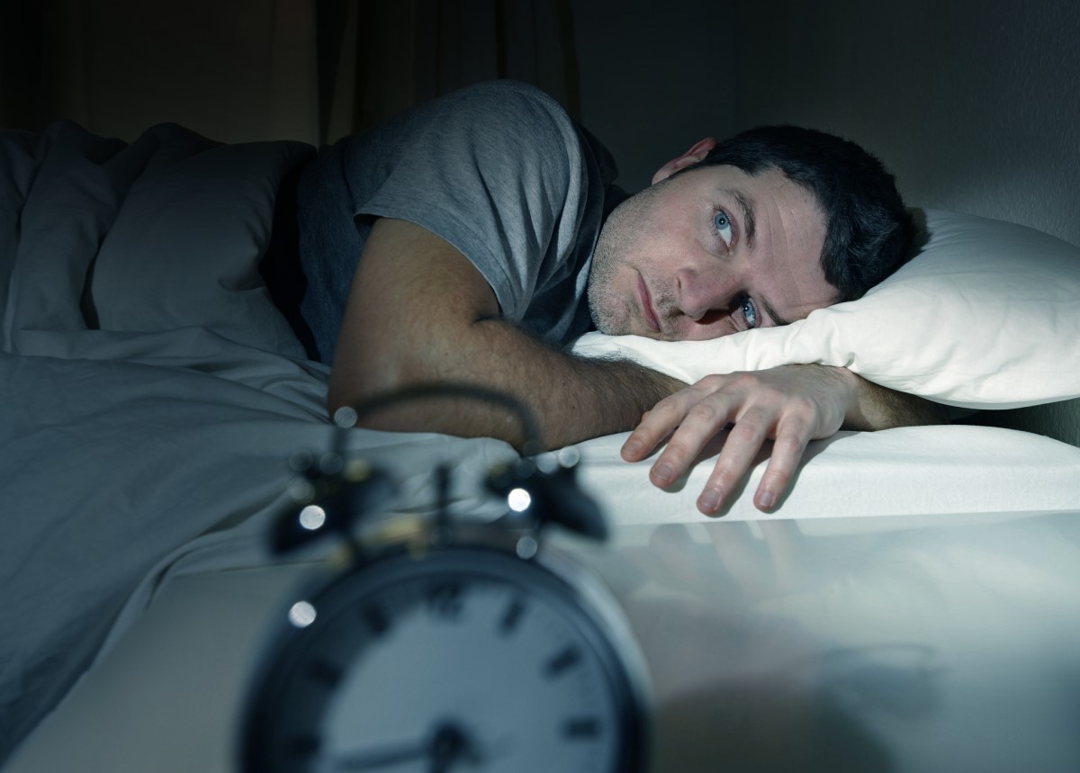 Perturbações do sono, homem deitado na cama a altas horas da noite e incapaz de adormecer, relógio sobre a mesa