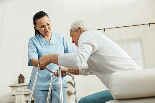 Restrição da mobilidade Fonte: Getty Images um idoso sentado numa cama de hospital a tentar levantar-se com a ajuda de um andarilho e de uma enfermeira
