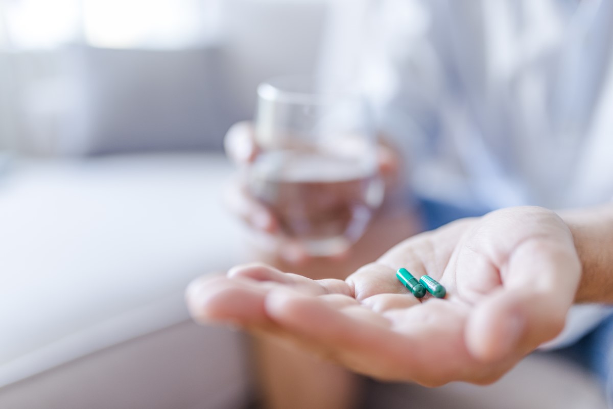 Medicamentos, comprimidos na mão do homem, na outra mão segura um copo de água para beber.