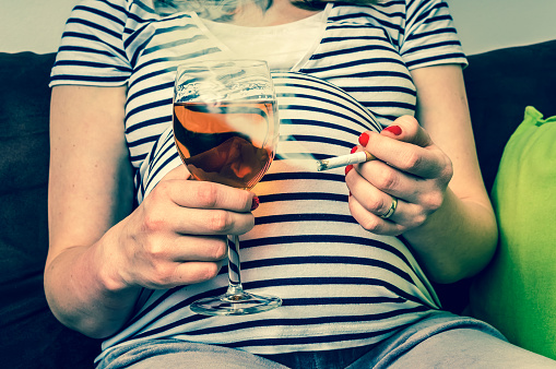 Substâncias que causam dependência. Foto: Getty Images Mulher grávida com uma T-shirt às riscas, um cigarro e um copo de vinho