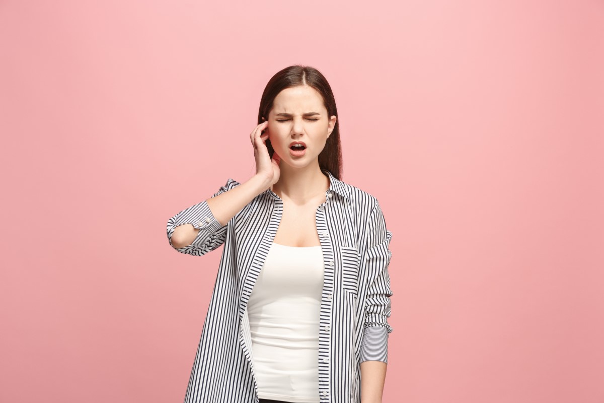 Nestes dois casos, a dor no ouvido é típica: Getty Images A orelha de uma mulher dói-lhe e ela está a segurá-la. Está de pé. Fundo cor-de-rosa.