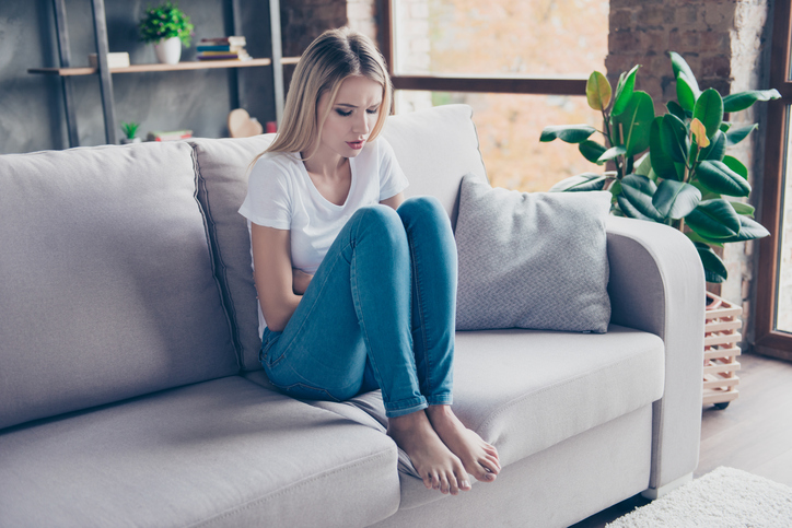 A dor pode ocorrer não só no abdómen, mas também na parte inferior das costas. Fonte: Thinkstock a mulher está a sofrer sentada no sofá