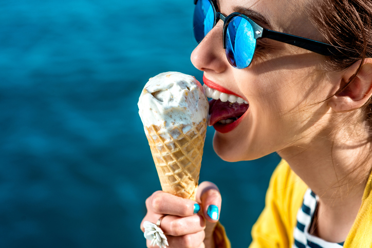 O frio provoca um choque no corpo quente, diminuindo as defesas do organismo e tornando-o mais suscetível a infecções. Foto: Thinkstock mulher de óculos de sol a lamber um gelado junto à água