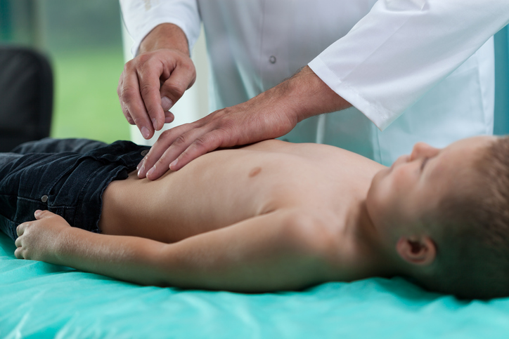 Nas crianças, durante a inflamação, após uma lesão, mas também devido ao stress: Getty Images A criança está deitada na mesa de exame, o médico examina-lhe o abdómen e ela tem dores
