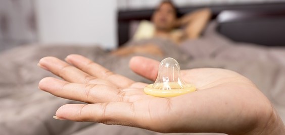 preservativo na mão de uma mulher, homem deitado na cama
