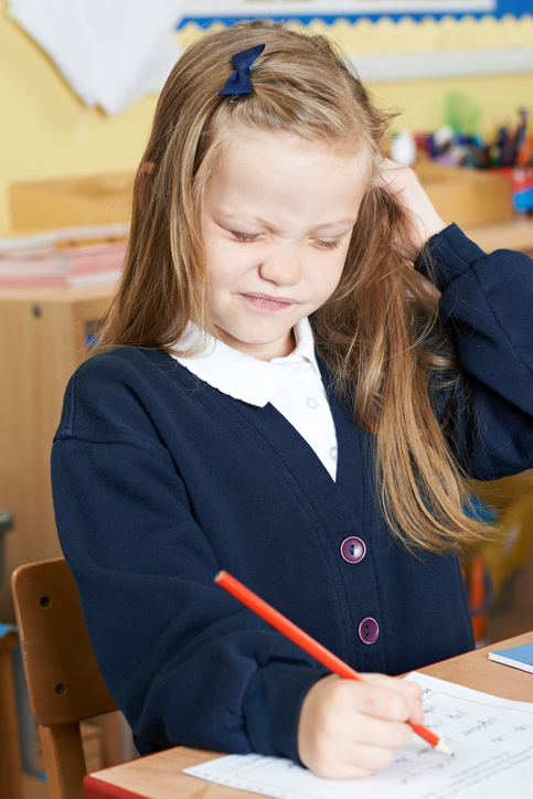 Os piolhos nas crianças causam perda de concentração. Fonte da foto: Thinkstock photos Uma menina sentada na escola com comichão na cabeça, provavelmente com piolhos no cabelo, cabelo loiro, sentada e a escrever