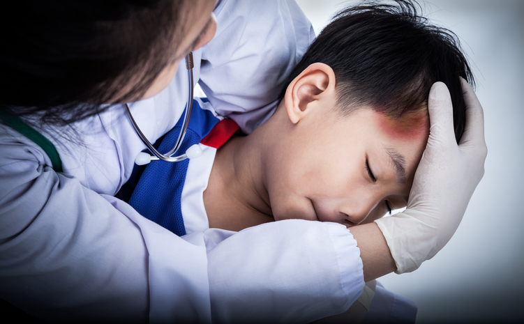 Mesmo depois de um traumatismo craniano, podem ocorrer estrabismo. Fonte da foto: Getty Images um rapazinho tem um ferimento na cabeça, a sua testa está ferida, um médico está a examiná-lo