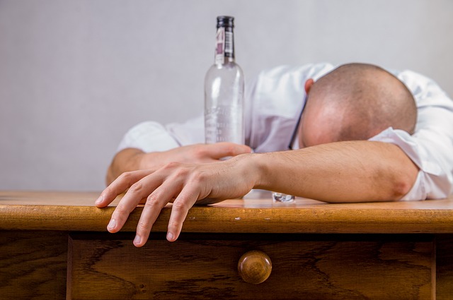 O alcoolismo é a causa das perturbações do humor, um homem deitado numa mesa com uma garrafa de álcool vazia, um alcoólico