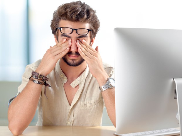 Trabalhar num computador durante muito tempo é uma das causas da síndrome do olho seco. Fonte da foto: Getty Images Homem mantém os olhos doridos, tem síndrome do olho seco por trabalhar num computador durante longos períodos de tempo