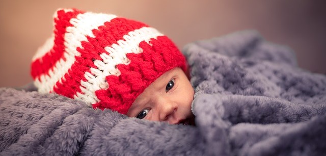 Nos recém-nascidos e bebés, é importante evitar a perda de calor. Fonte da foto: Getty Images Uma criança, deitada e coberta, com um gorro às riscas vermelhas e brancas