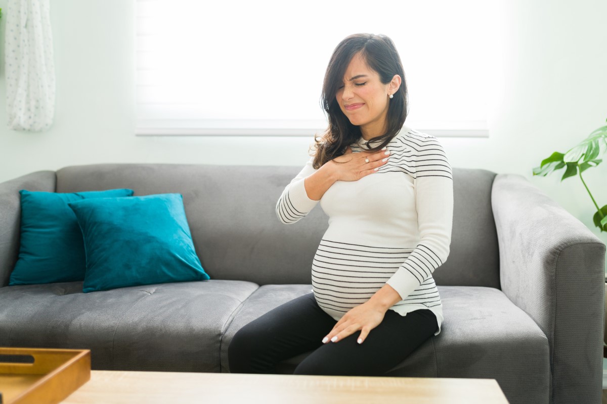 A azia é comum nas mulheres grávidas. Fonte da foto: Getty Images A azia é comum nas mulheres grávidas - uma mulher grávida senta-se num sofá e segura o peito