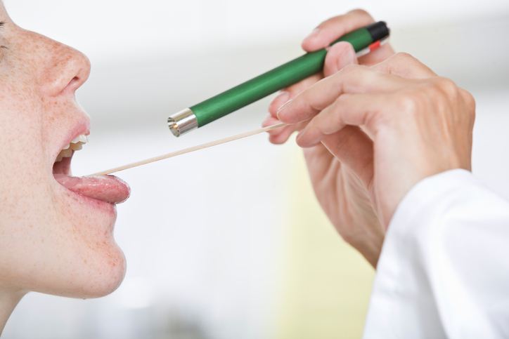 Em caso de dor persistente, é necessário efetuar um exame. Foto: Getty Images o médico examina a garganta da mulher com um bocal e os seus olhos, fazendo passar uma lanterna pela garganta