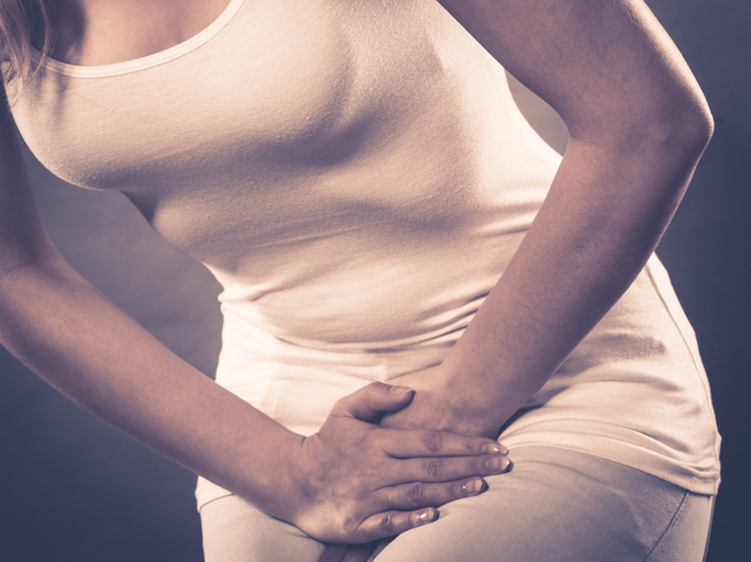 A causa pode ser uma inflamação, quer do sistema urinário quer do sistema genital. Fonte da foto: Thinkstock photos Mulher segura a virilha, com dores devido a problemas urinários e genitais, inflamação