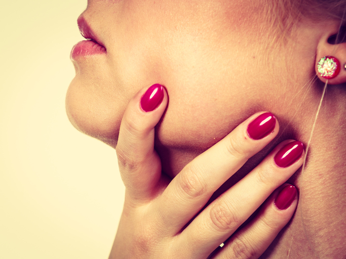 Angina é o nome dado a uma dor incómoda... Foto: Getty Images A mulher está a segurar a garganta, que lhe dói, as unhas estão pintadas de vermelho