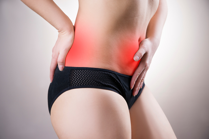 A dor irradia frequentemente para várias zonas, incluindo o sacro: Getty Images uma mulher segura a parte inferior do abdómen e a zona sacral onde a dor se irradia tem dores ovulatórias